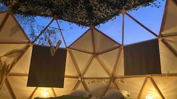 A tented accommodation with a geometric structure, two beds with pillows, and hanging decorations.