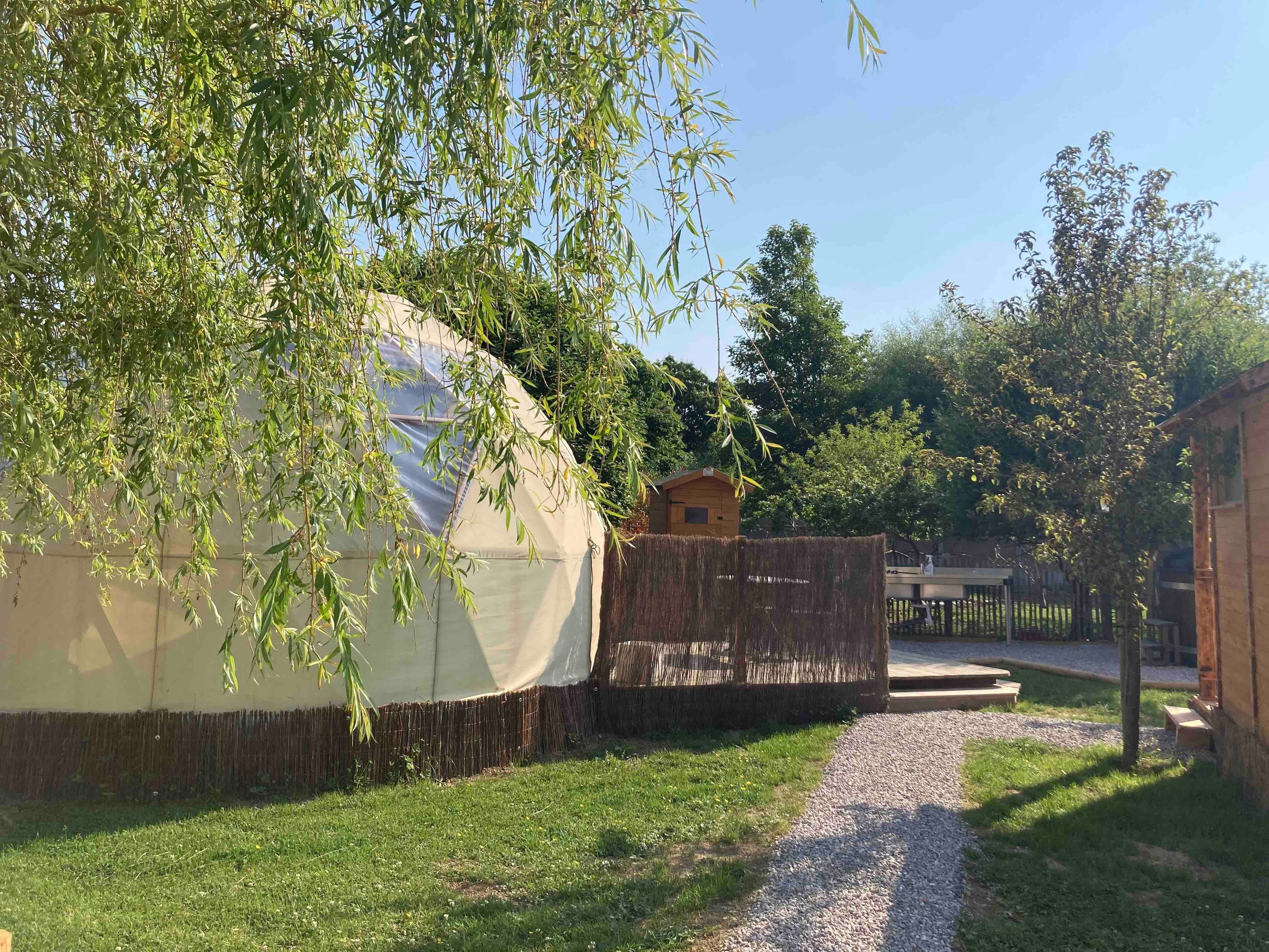 A yurt with a straw-covered base, a wooden structure, and a gravel path leading to it.