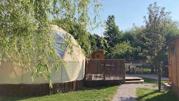 A yurt with a straw-covered base, a wooden structure, and a gravel path leading to it.