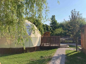 A yurt with a straw-covered base, a wooden structure, and a gravel path leading to it. - Dome 'Le Trou Du Charme - Le Dome, terasse et jardin' (Bournonville)