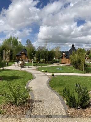 A pathway leading to wooden cabins with a grassy area and trees in the background.