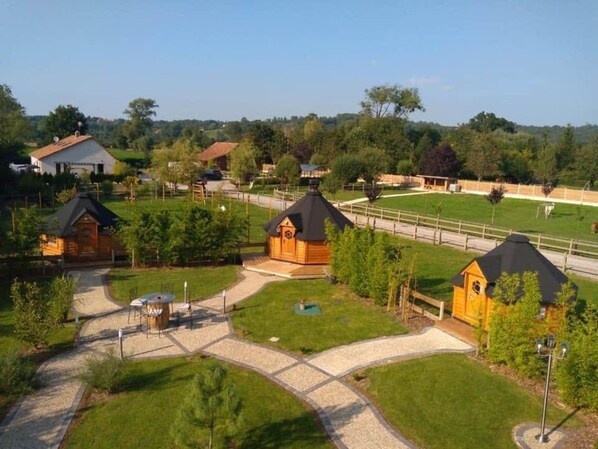 A residential area with multiple wooden houses, a paved driveway, and a fenced sports field.
