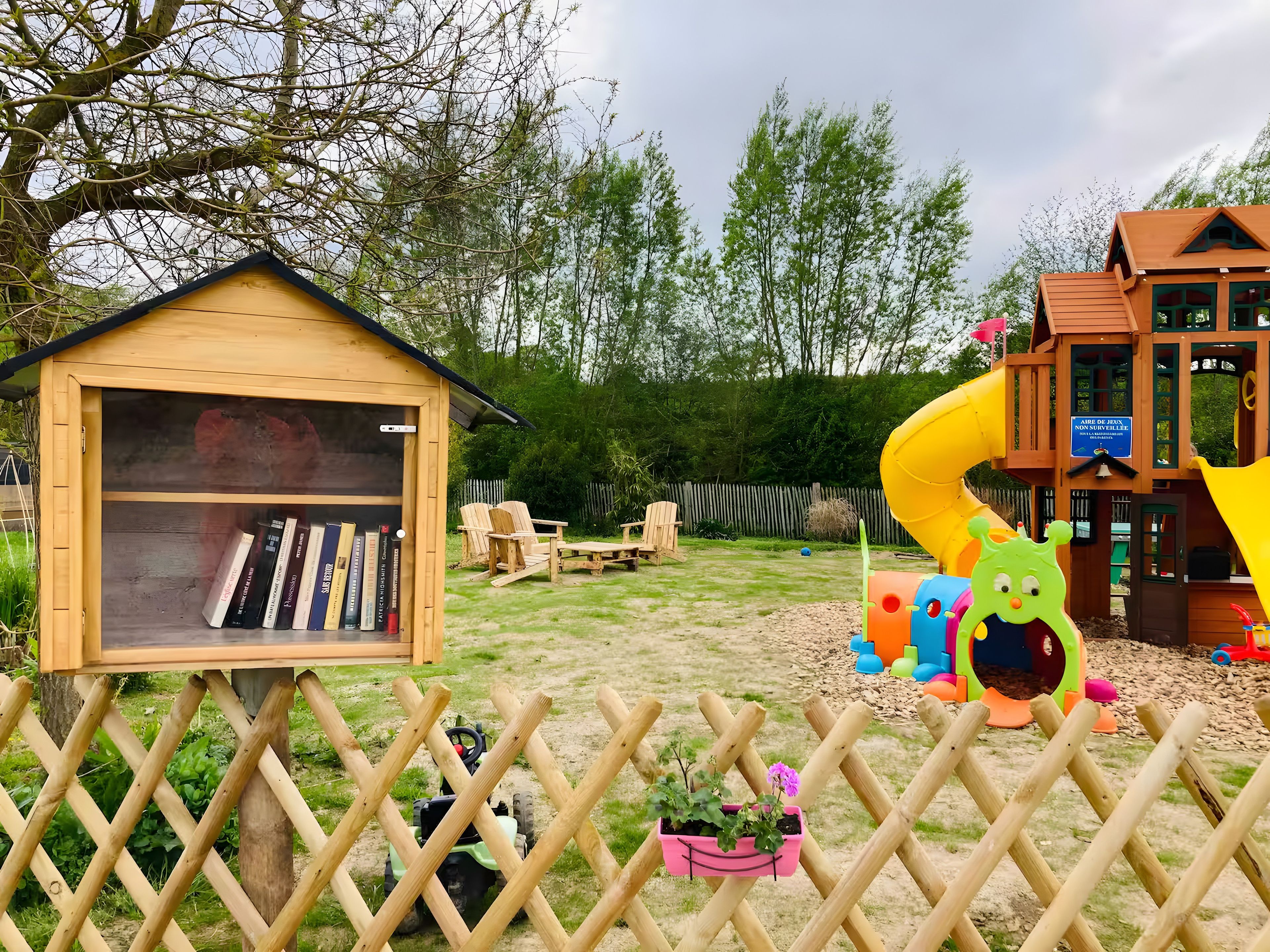 Een houten poppenhuis met een boekenkast, een glijbaan en een speelruimte vol speelgoed.