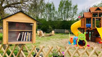 Een houten poppenhuis met een boekenkast, een glijbaan en een speelruimte vol speelgoed.