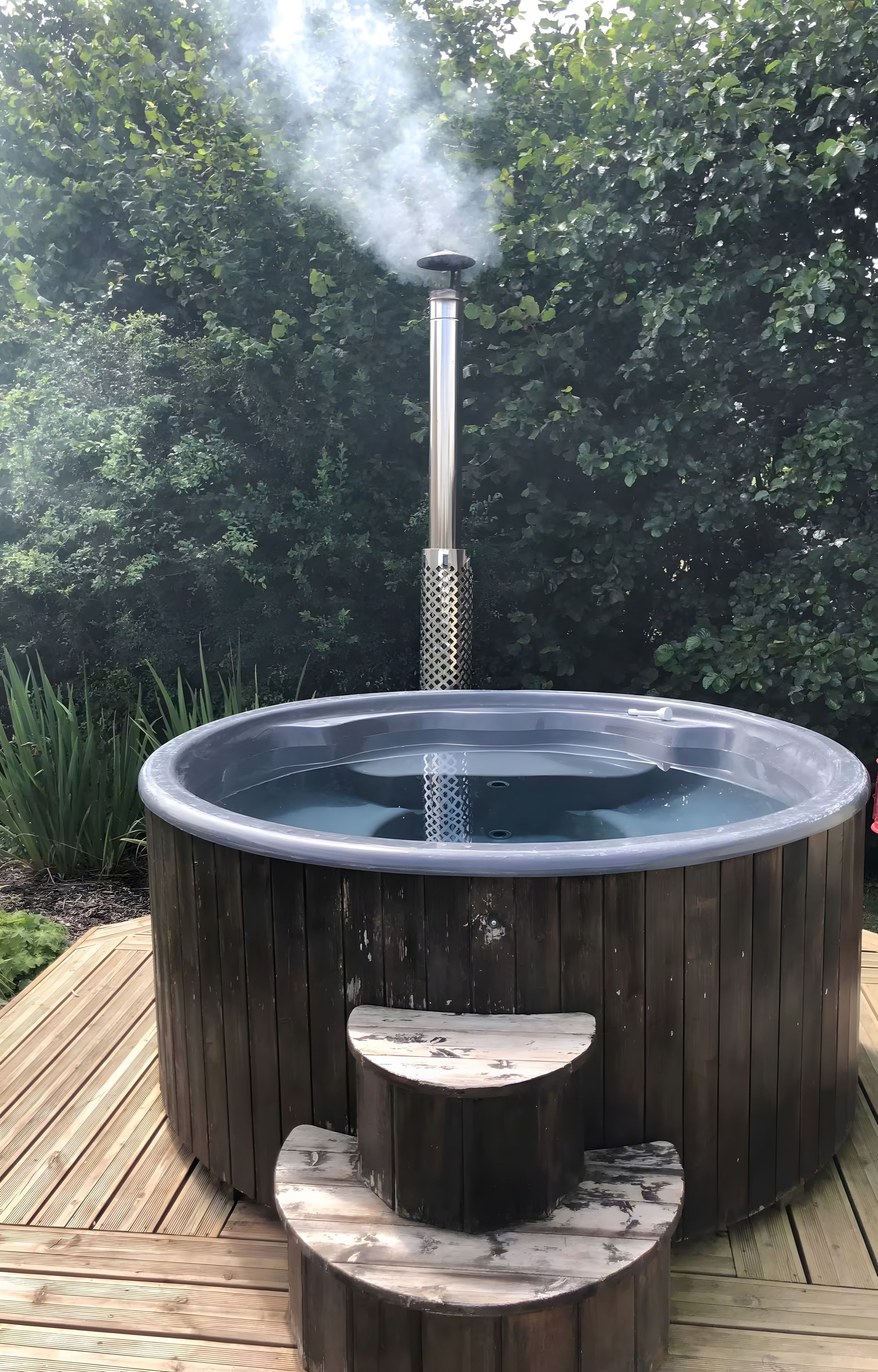 Un bain à remous sur une terrasse en bois, entouré de verdure.