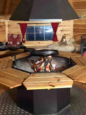 Ein hexagonales Feuerkorb mit schwarzem Unterteil und Holzsitzen darum herum.