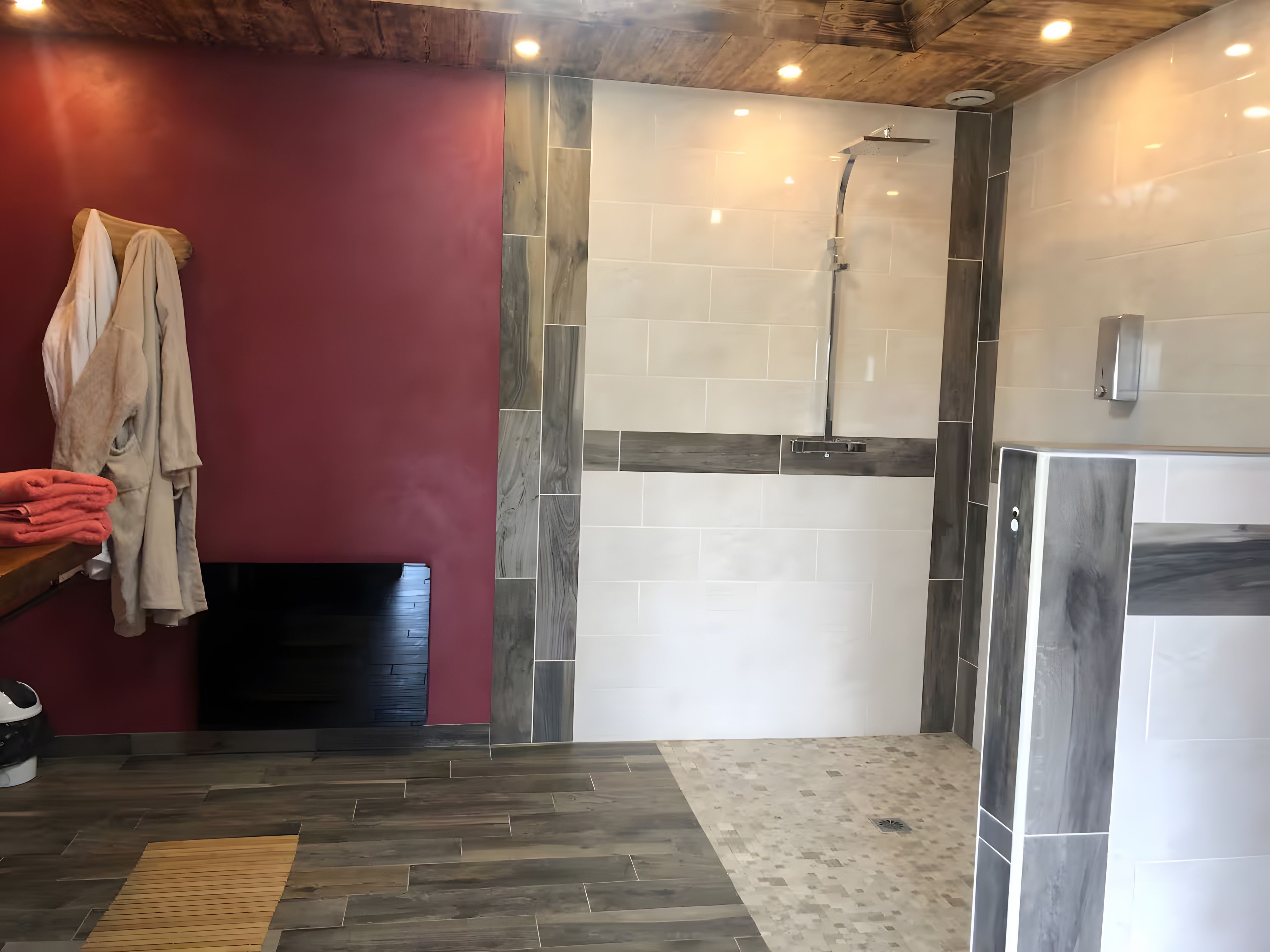 Une salle de bain avec un plancher en bois, un mur rouge et un espace douche dont les murs sont recouverts de carreaux.
