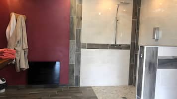 Une salle de bain avec un plancher en bois, un mur rouge et un espace douche dont les murs sont recouverts de carreaux.
