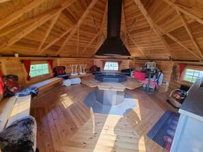 A spacious wooden interior with a central seating area, a fireplace, and a window providing natural light.
