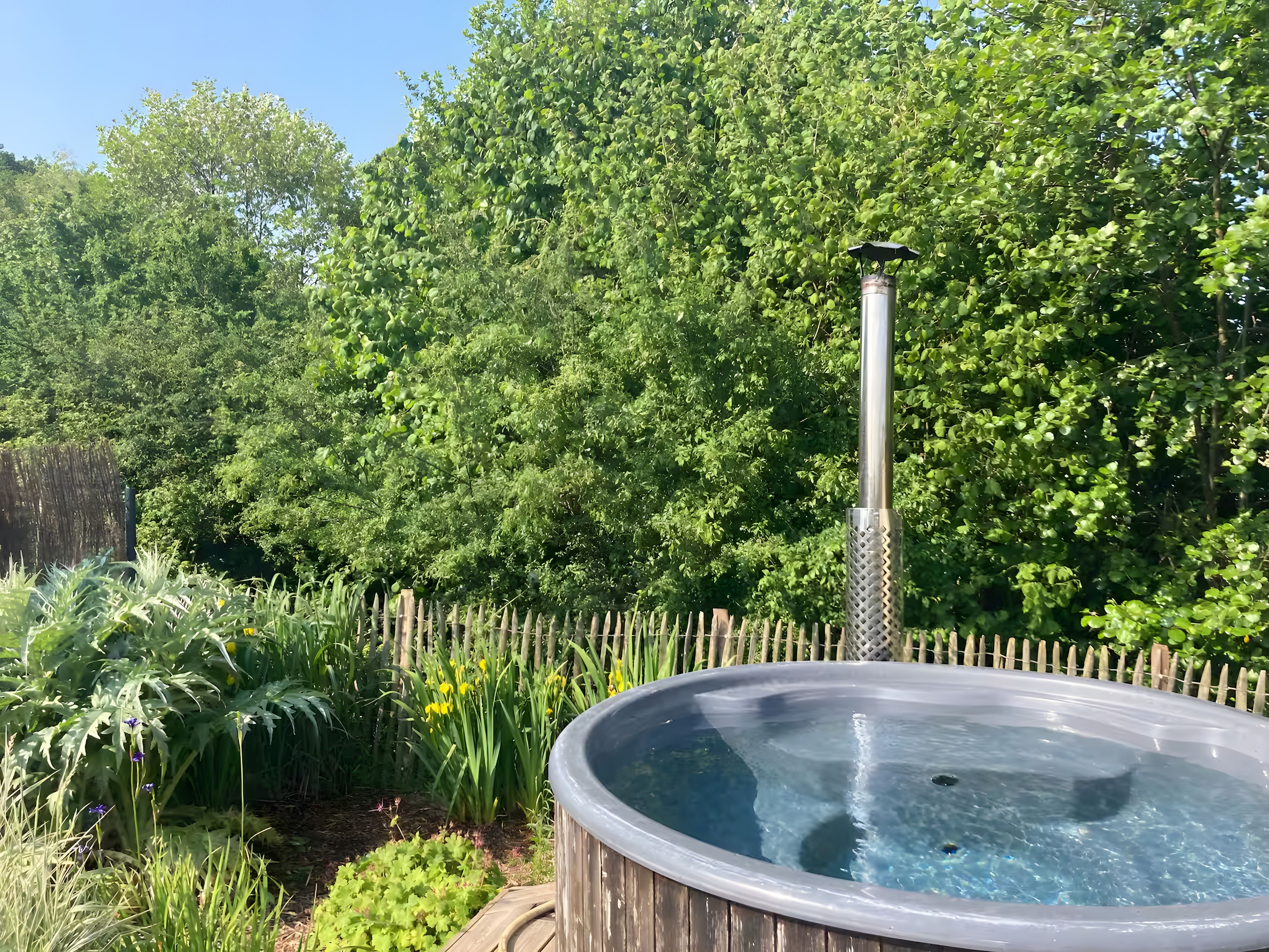 Un bain à remous entouré d’une végétation luxuriante et délimité par une clôture en bois.
