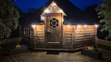 Eine Holzhütte mit einer sechseckigen Tür, einem geneigten Dach und einer Veranda mit Pflanzgefäßen.