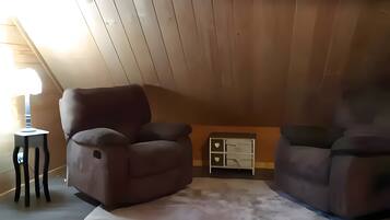 A room with a sloped ceiling, two brown armchairs, a small white table, and a white cabinet.