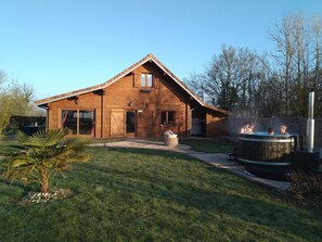 A wooden house with a sloped roof, a hot tub, and a well-maintained lawn.