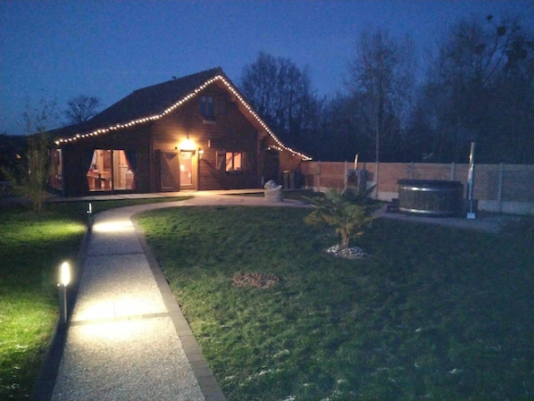 A house with a well-lit entrance, a paved driveway, and a small lawn area.