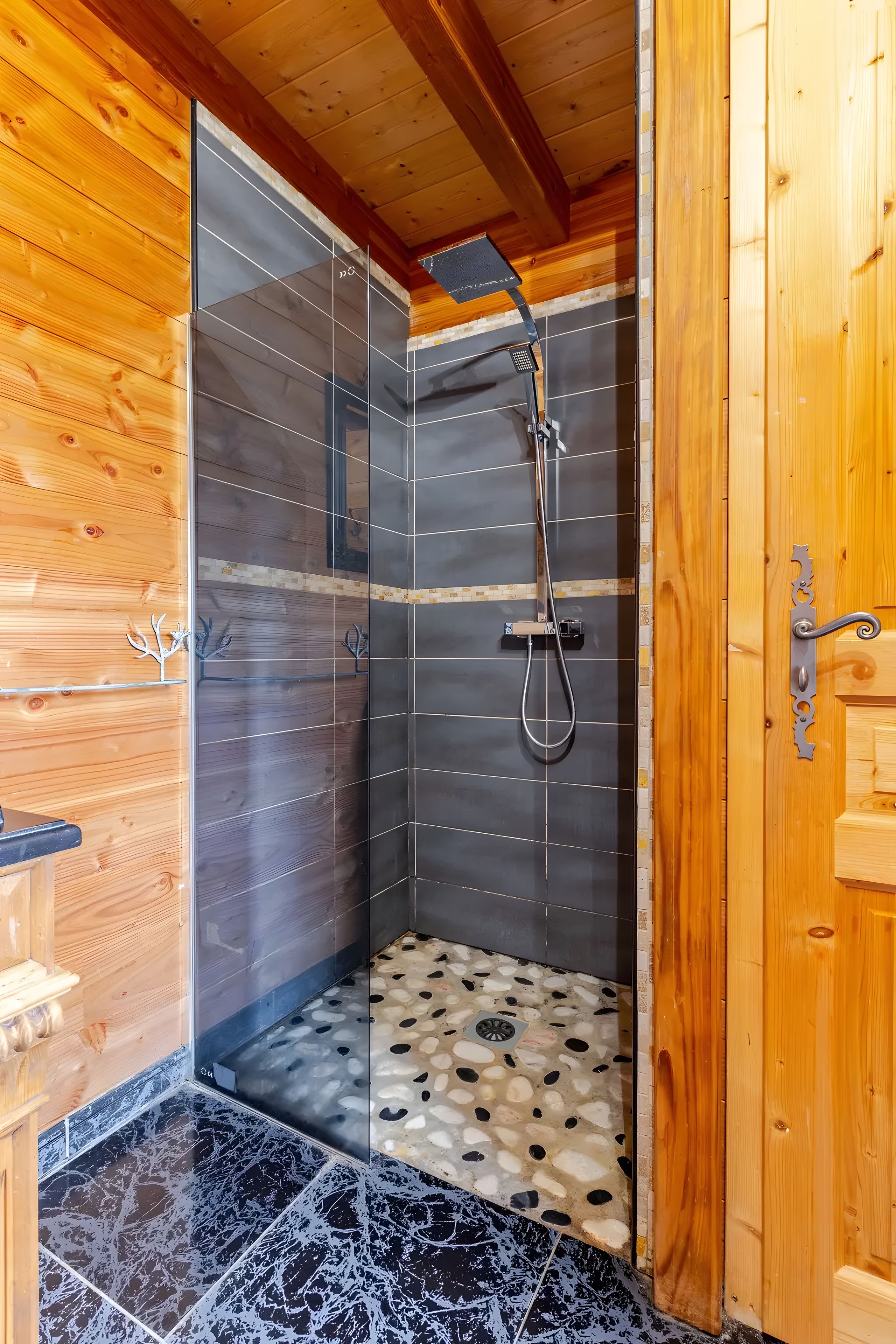 Una cabaña de madera con zona de ducha, paredes con azulejos y suelo de diseño de guijarros.