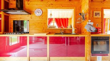Een keuken met houten wanden, een rode kast, een fornuis, een magnetron en een klok aan de muur.