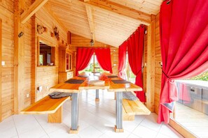 A wooden cabin with a central dining table, benches, and red curtains.