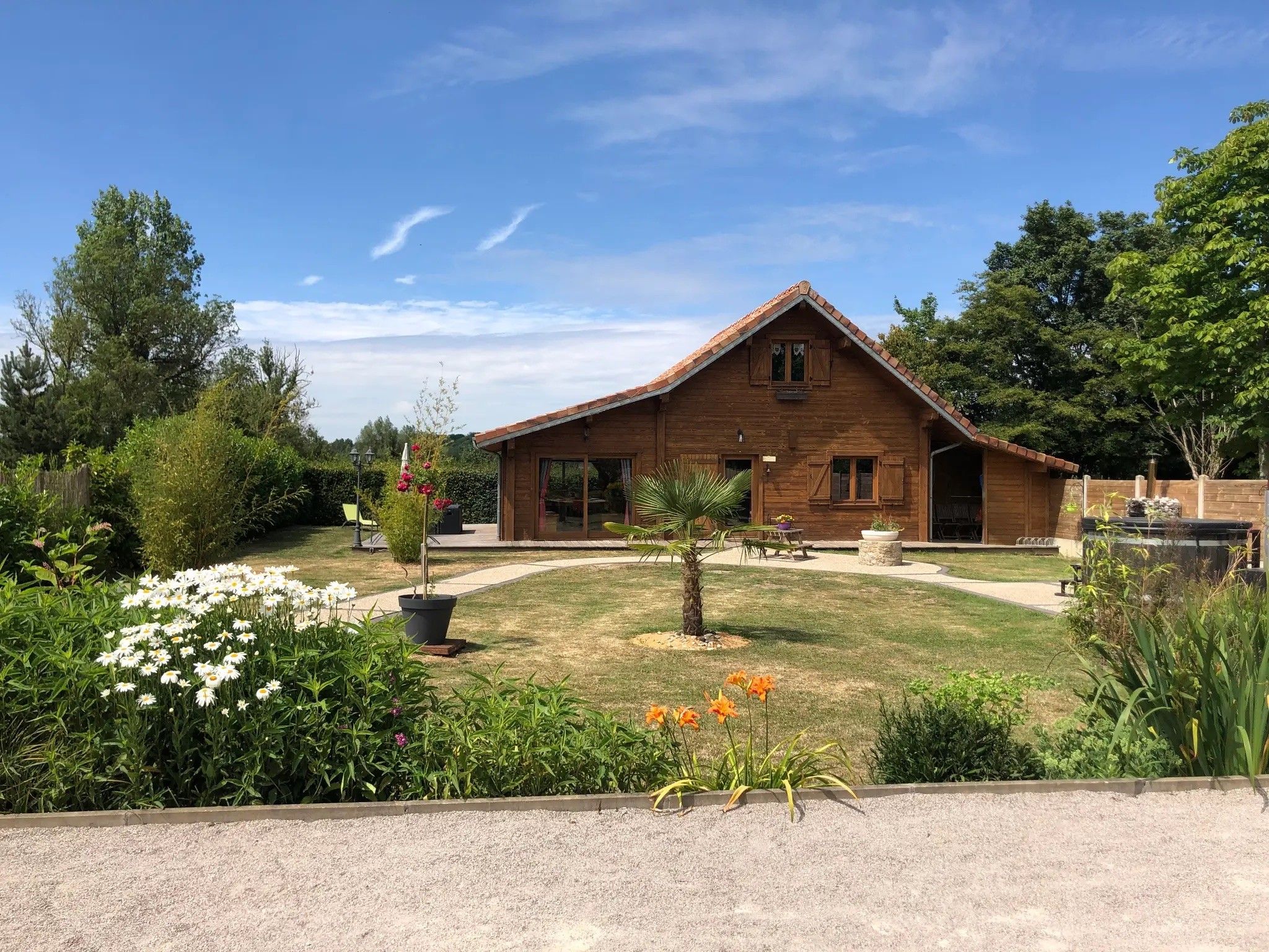 Une maison en bois avec un toit en pente, entourée d’un jardin bien entretenu où poussent différentes plantes et fleurs.