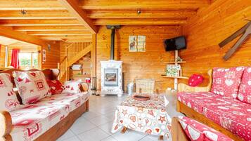 Een gezellig chaletinterieur met houten wanden, een open haard, een televisie en een eethoek.