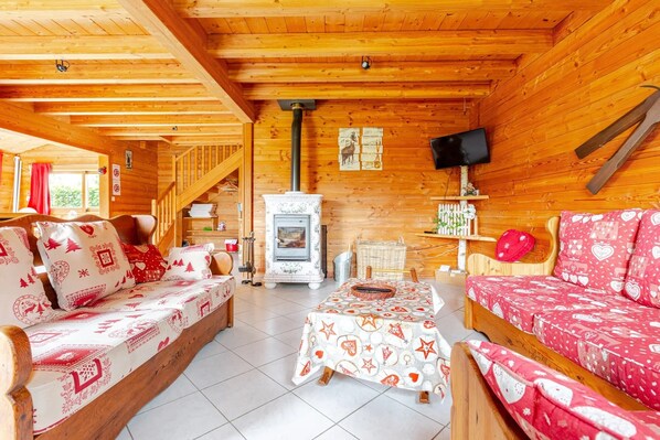 A cozy cabin interior with wooden walls, a fireplace, a television, and a dining area.