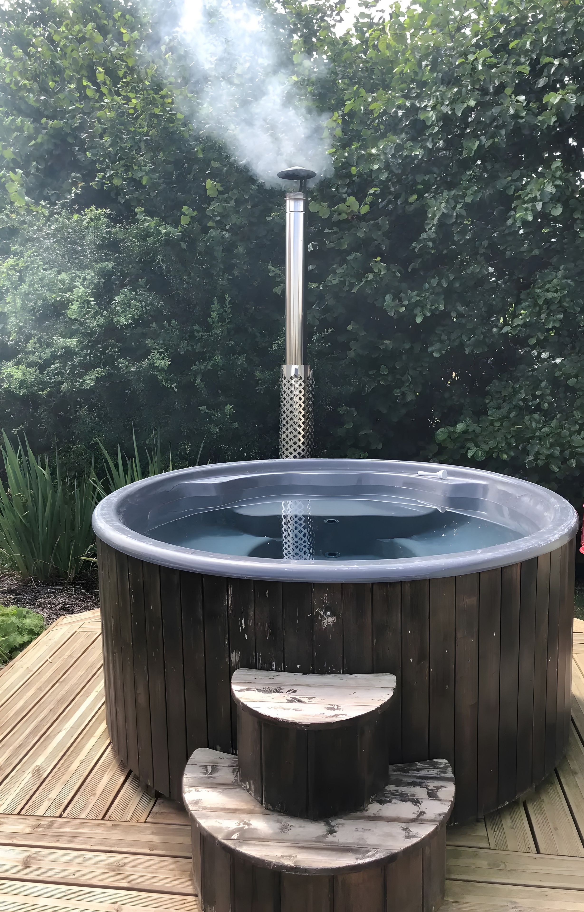 Een hottub met stoomfunctie, omringd door een houten terras en groen.
