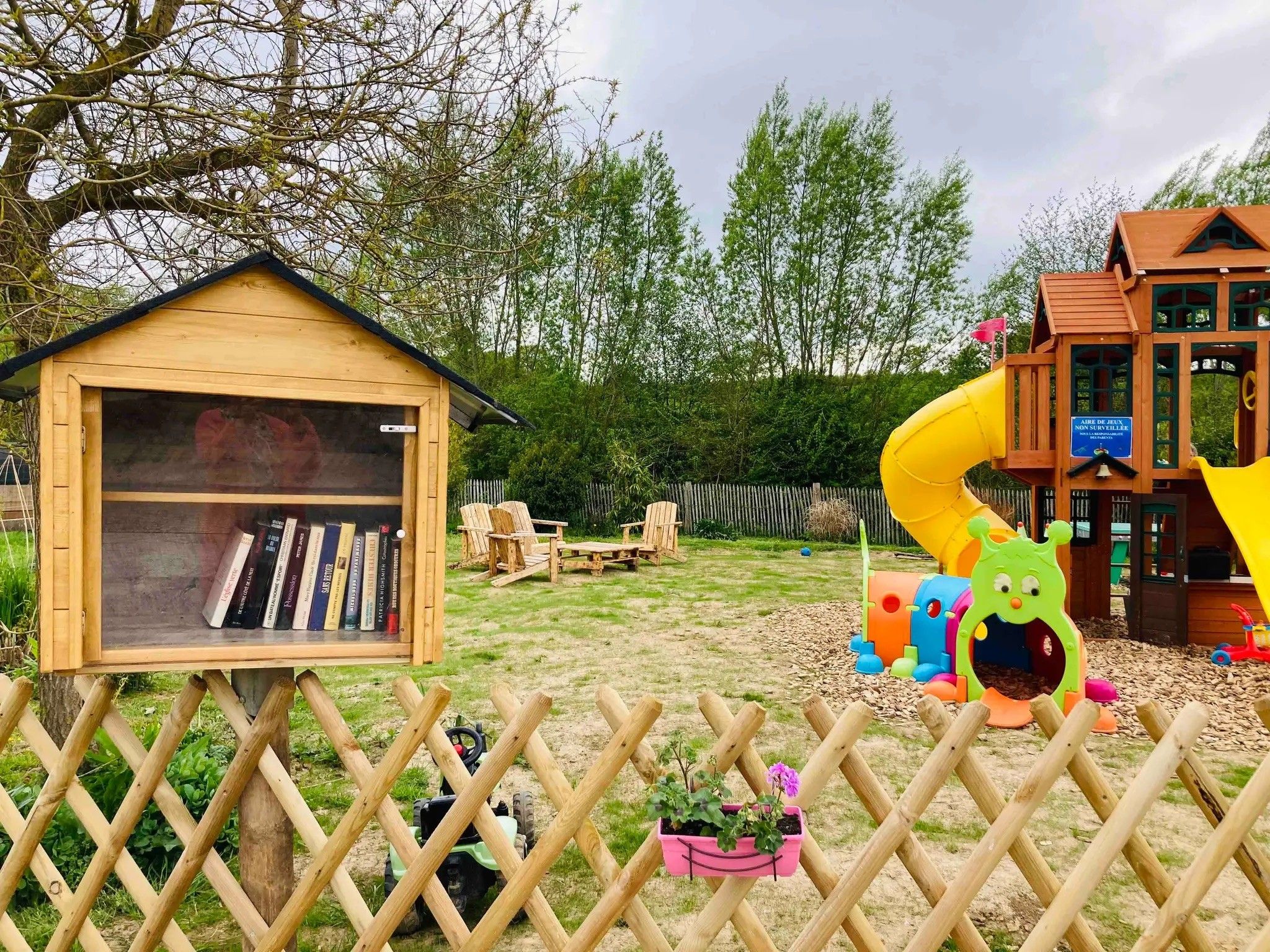 Een houten poppenhuis met een boekenkast, een glijbaan en een speelgedeelte met een figuur van een groen wezen.