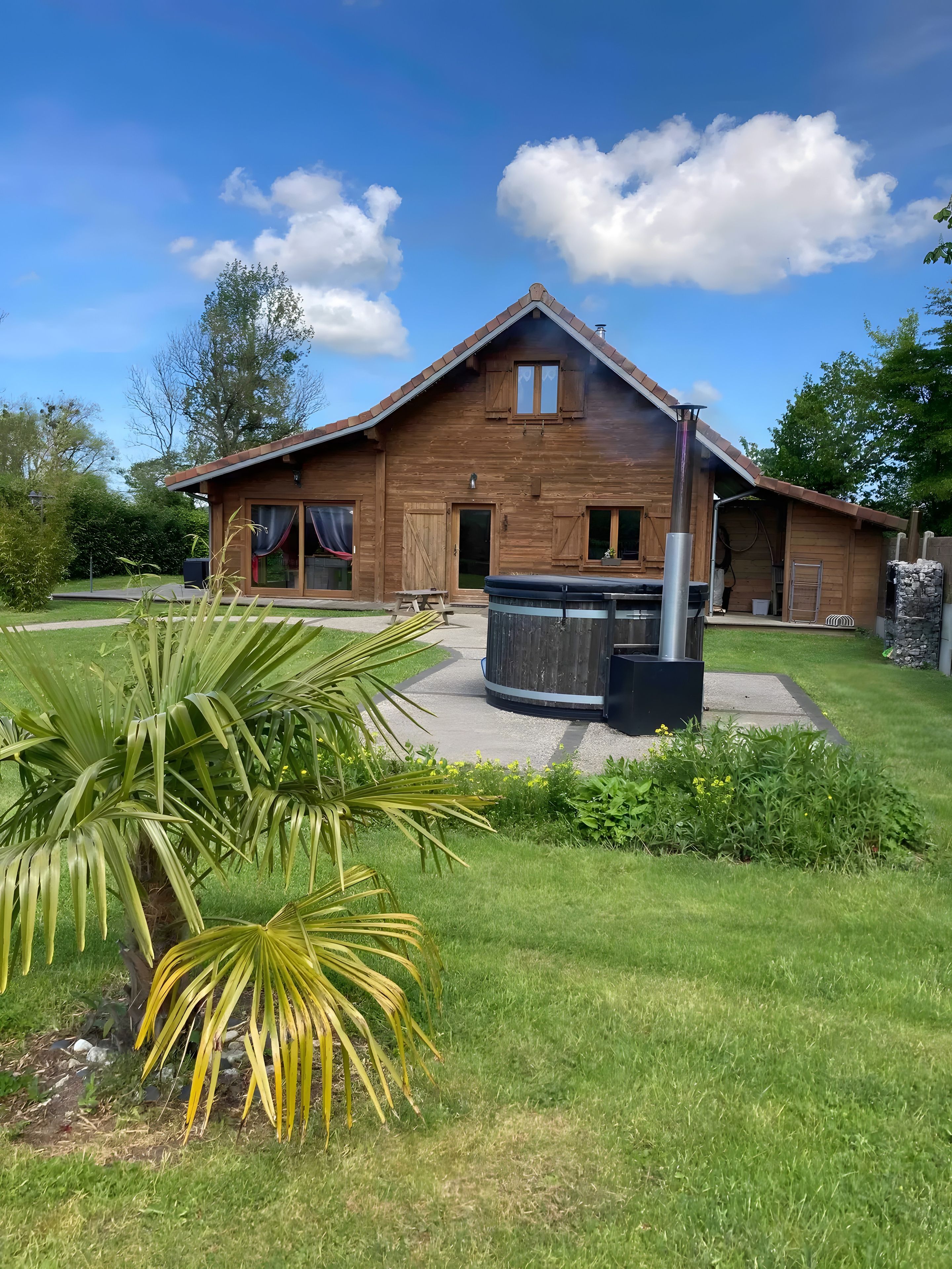 Een houten huis met een terras, een jacuzzi en een verzorgd gazon.