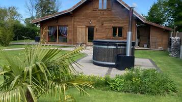 Een houten huis met een terras, een jacuzzi en een verzorgd gazon.