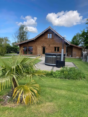 A wooden house with a patio, a hot tub, and a well-maintained lawn.