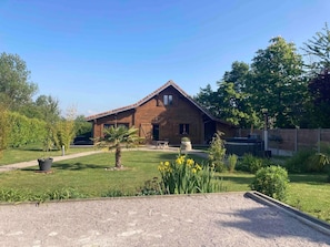 A wooden house with a sloped roof, surrounded by a well-maintained lawn and garden.