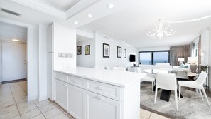 A modern kitchen with white cabinetry, a central island, and a dining area with white chairs. - 406 Sandcastle in Ponce Inlet, FL (Ponce Inlet)