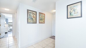A hallway with two framed vintage advertisements on the wall, a door leading to a room, and a tiled floor. - 406 Sandcastle in Ponce Inlet, FL (Ponce Inlet)