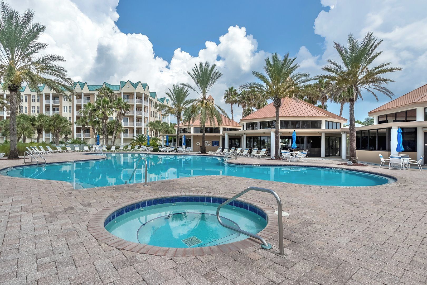 A swimming pool with lounge chairs and palm trees, surrounded by multi-story buildings with balconies.