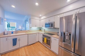 A modern kitchen with stainless steel appliances, white cabinetry, and a wooden floor. - 4404 Harbour Village (Ponce Inlet)