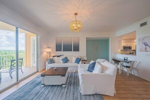 A modern living room with a sectional sofa, a coffee table, and a dining area with a table and chairs. There is a balcony with a view of the landscape. - 4404 Harbour Village (Ponce Inlet)