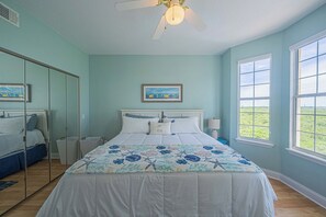 A bedroom with a bed, a ceiling fan, a window with a view, and a painting on the wall. - 4404 Harbour Village (Ponce Inlet)