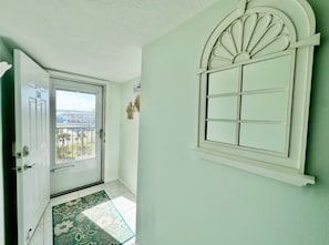 Un passadís amb una porta que dona a un balcó, una finestra amb un marc decoratiu i una catifa amb dibuixos al sòl.
