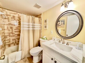 A bathroom with a bathtub, toilet, and a sink with a mirror. - #504 Tide Water Oceanview Condo (Ponce Inlet)