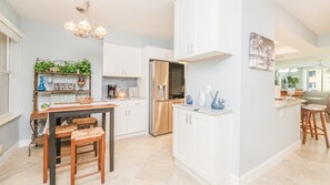 A modern kitchen with white cabinetry, a dining area with a wooden table and chairs, and a kitchen island with bar stools. - #5111 Towers @ Ponce Inlet 2/2 Oceanfront Condo Traffic Free Beach (Ponce Inlet)