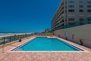 A swimming pool with a view of the beach and ocean, surrounded by a building with multiple floors. - #5111 Towers @ Ponce Inlet 2/2 Oceanfront Condo Traffic Free Beach (Ponce Inlet)