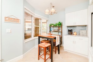 A kitchen with white cabinets, a wooden table, and two stools. - #5111 Towers @ Ponce Inlet 2/2 Oceanfront Condo Traffic Free Beach (Ponce Inlet)