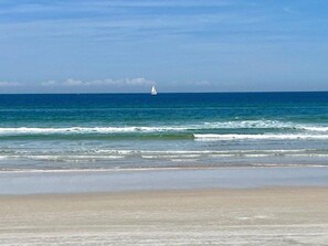 A beach with a sailboat in the distance, calm sea, and clear sky. - 5203 Towers in Ponce Inlet, FL (Ponce Inlet)