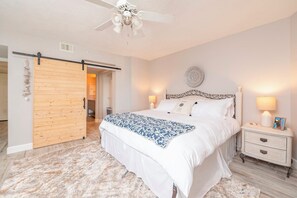 A bedroom with a bed, bedside tables, a ceiling fan, and a wooden door. - 5203 Towers in Ponce Inlet, FL (Ponce Inlet)