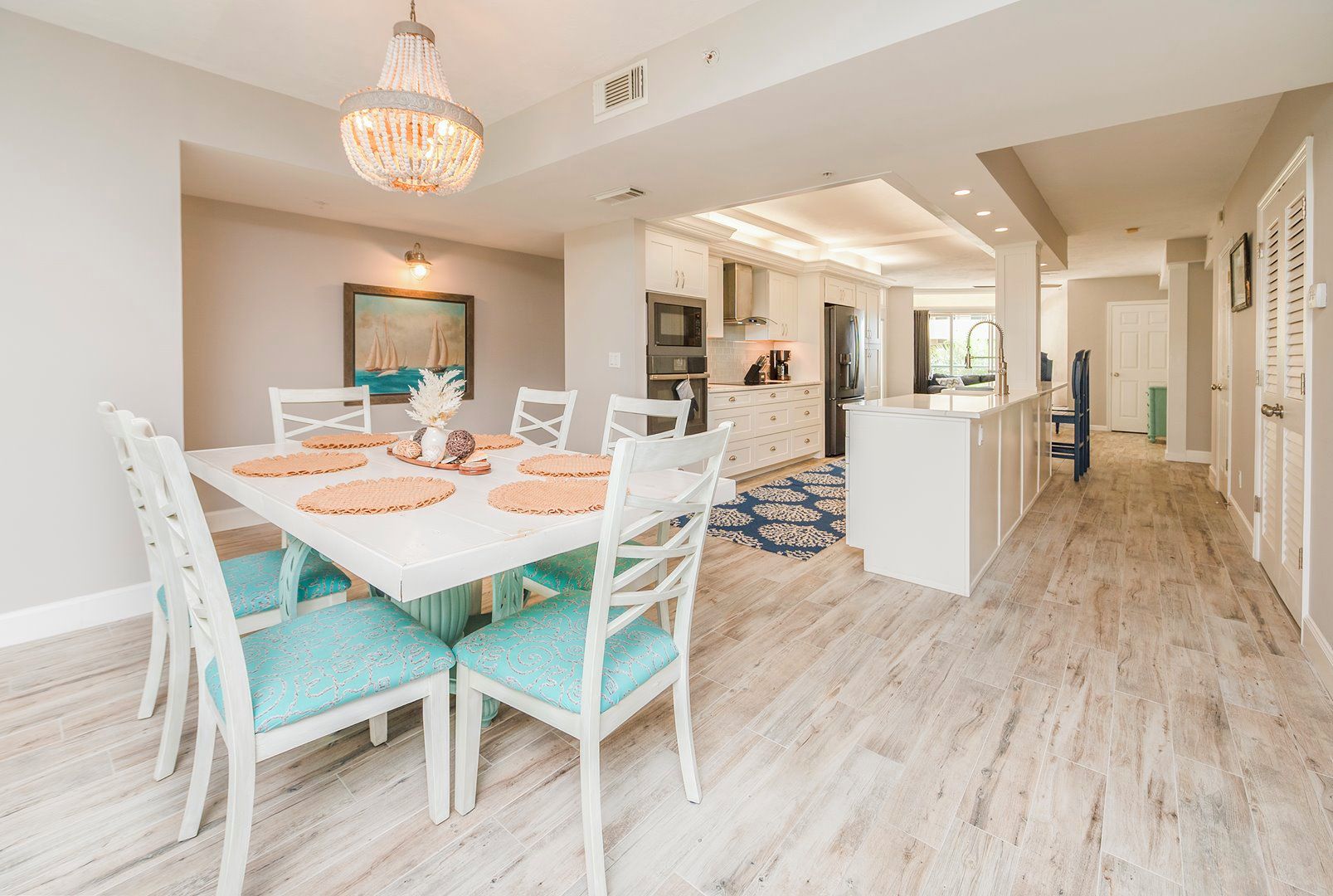 A modern kitchen with white cabinets, a central island, and a dining area with a white table and chairs.