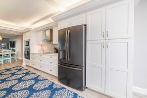 Une cuisine moderne avec des meubles blancs, un réfrigérateur noir et un tapis à motifs bleus.