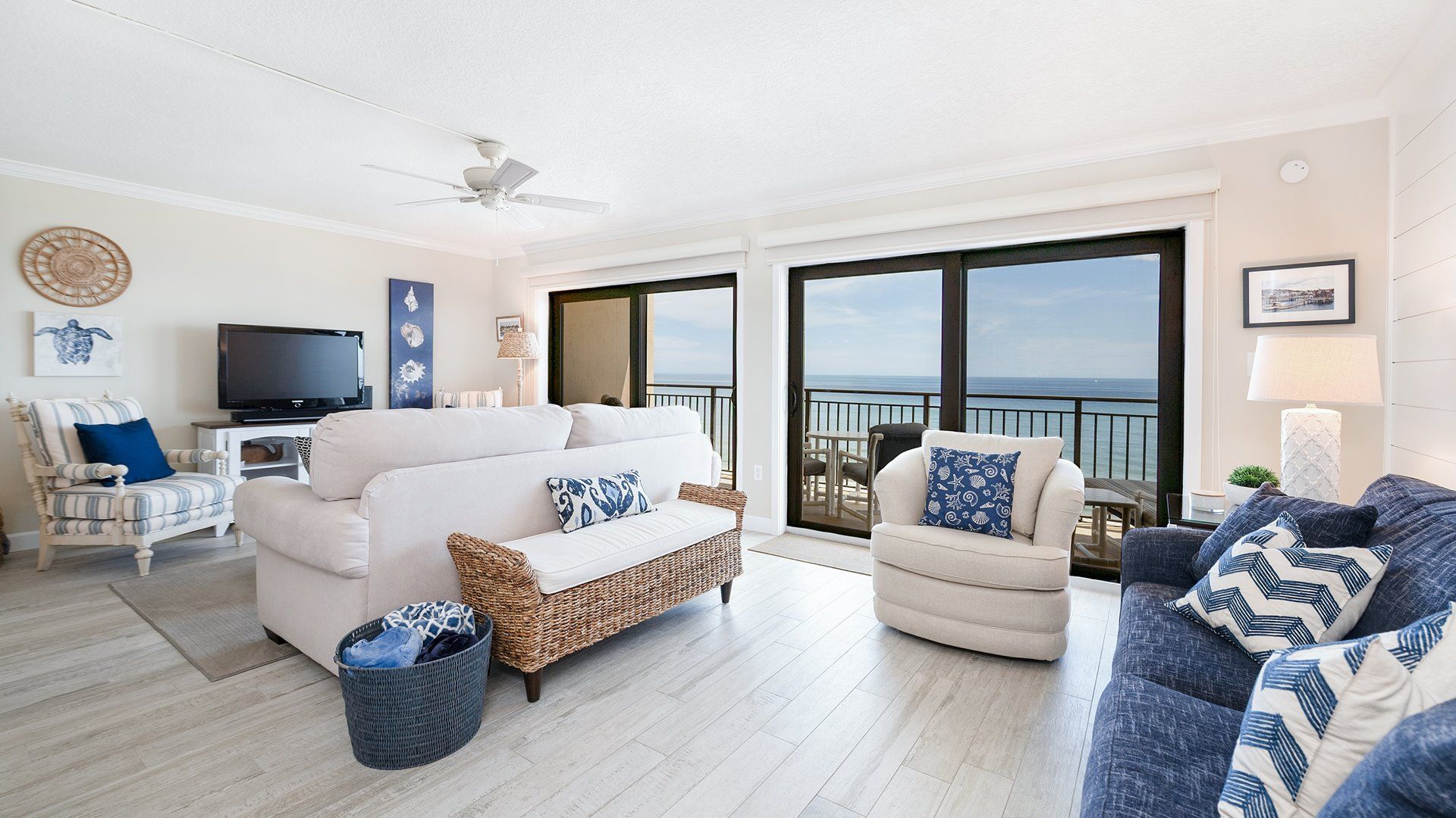 A spacious living room with a large sofa, a television, and a view of the ocean through large windows.
