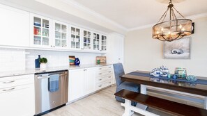 A kitchen with white cabinets, a dishwasher, a wooden bench, and a hanging light fixture. - 602 Sand Castle So in Ponce Inlet, FL (Ponce Inlet)