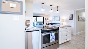 A modern kitchen with stainless steel appliances, a central island, pendant lighting, and a view to the living area. - 602 Sand Castle So in Ponce Inlet, FL (Ponce Inlet)