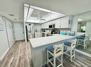 A modern kitchen with a central island, white cabinetry, and a ceiling fan. - #604 Blue Surf 2/2 Oceanfront Condo On Traffic Free Beach (Daytona Beach Shores)