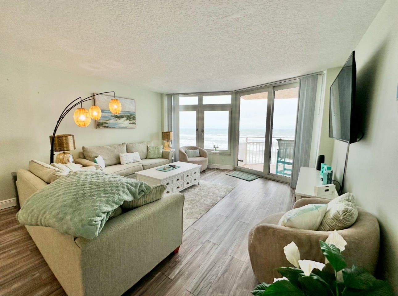 A spacious living room with a large window, a flat-screen TV mounted on the wall, and a comfortable seating area with a sofa and armchairs.